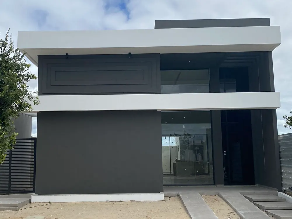 Foto da casa construída, com volume escuro e marquise branca